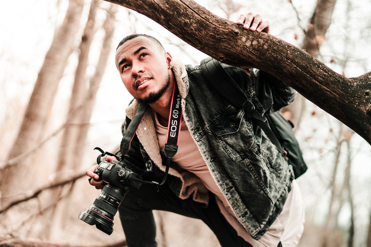 man holding camera while holding on to tree branch