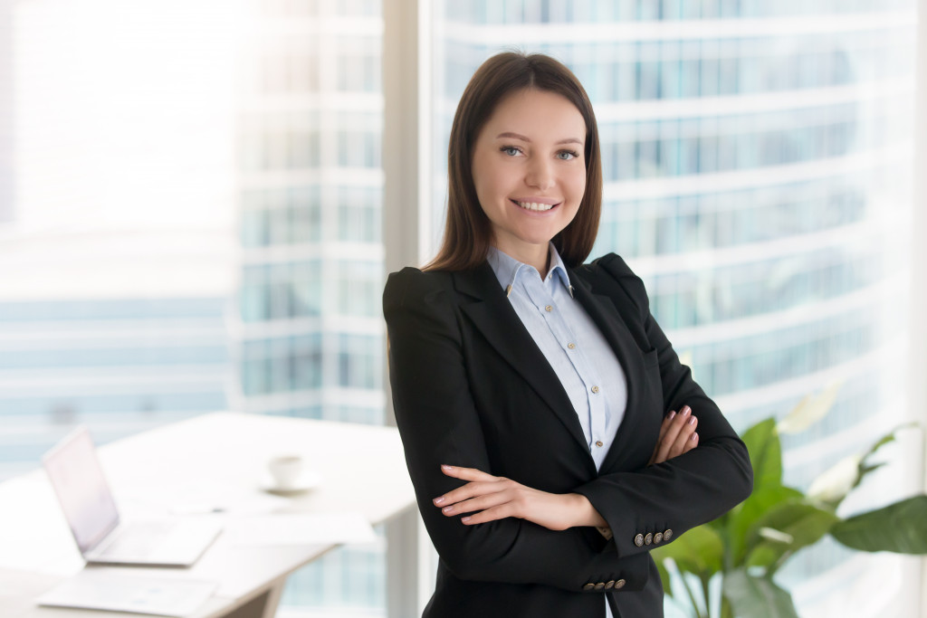A successful female company executive smiles at the camera with her hands folded against her body