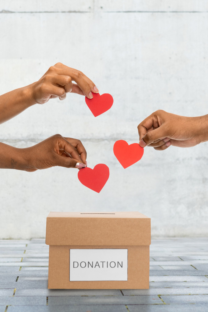 A concept photo of hands placing heart-shaped coins into a donation box