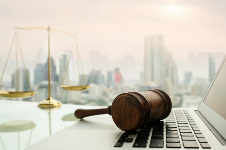 gavel on top of a laptop keyboard with justice scale and buildings in the background